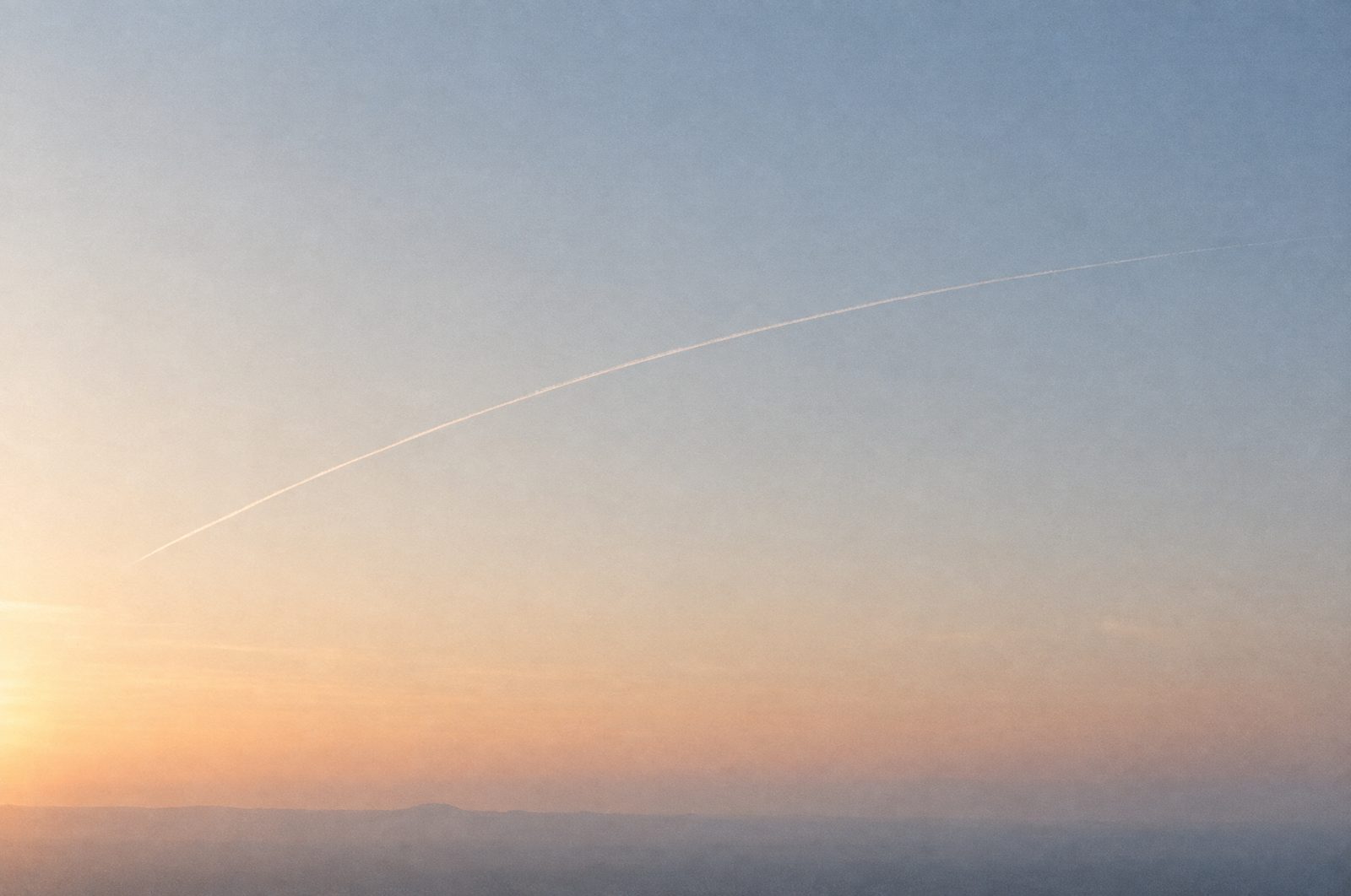 A single contrail arcing across a pale dawn sky